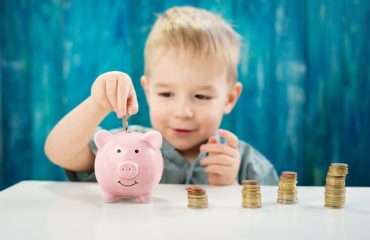 three years old child sitting st the table with money and a piggybank