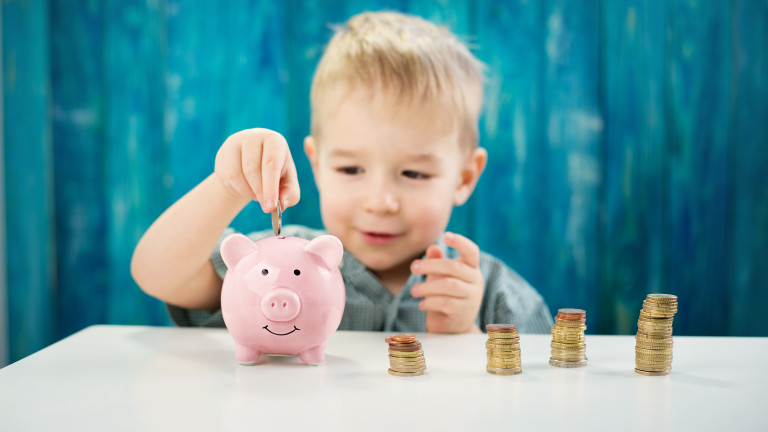 three years old child sitting st the table with money and a piggybank